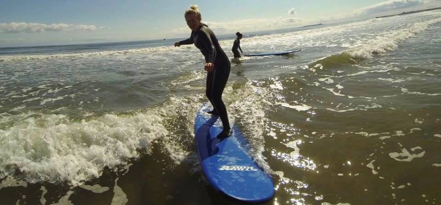 Person surfing on a blue surfboard in the ocean, with another surfer in the background.